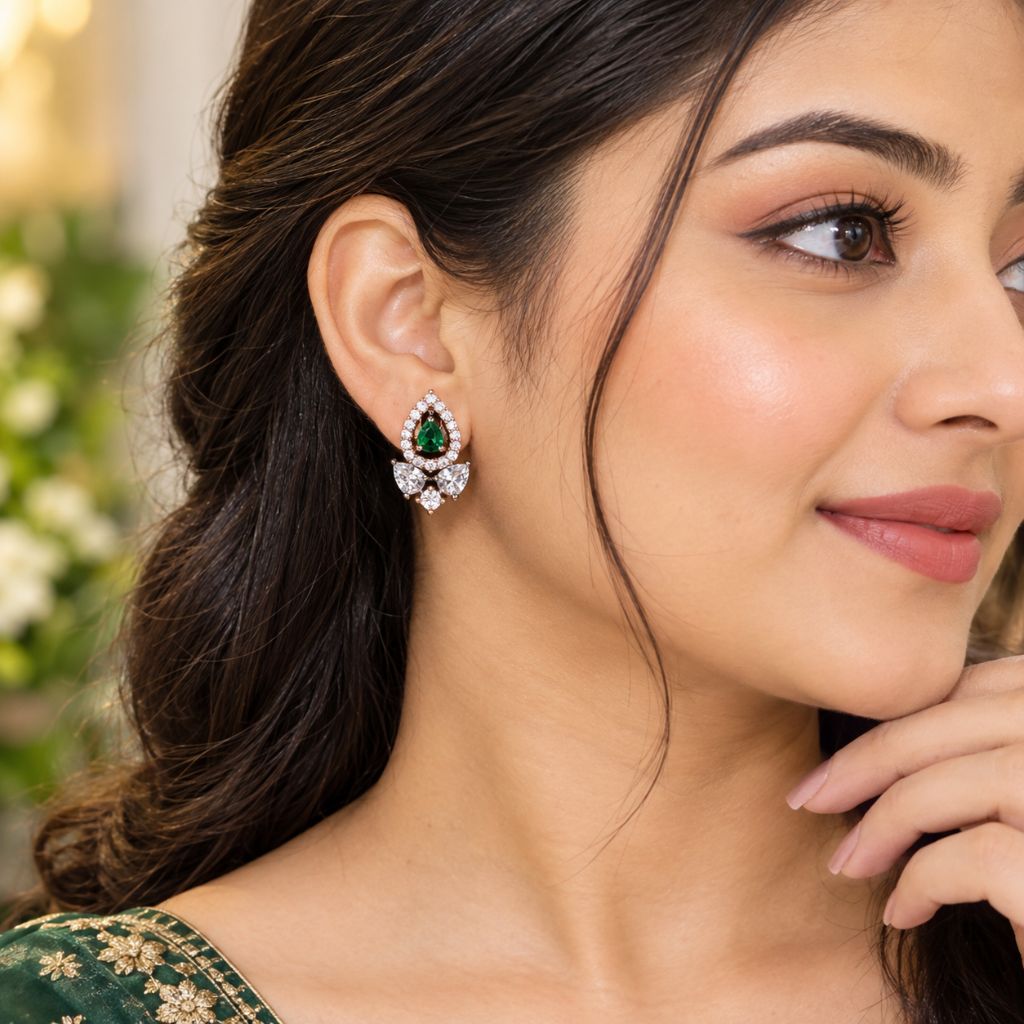 A close-up of a woman wearing a teardrop-shaped green stone and diamond stud earring, shown in profile against a softly blurred background.