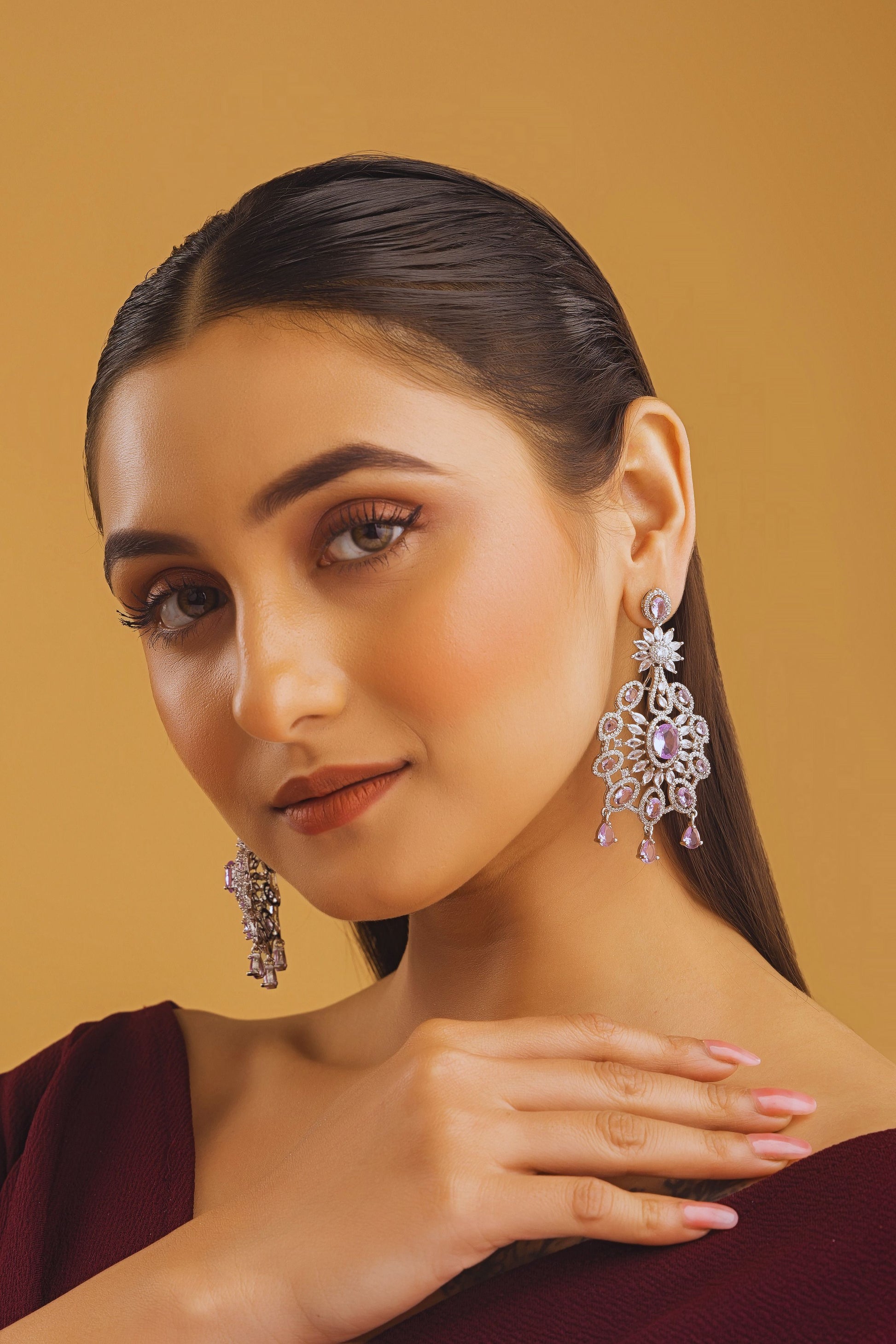 Woman wearing intricate earrings against a warm brown background