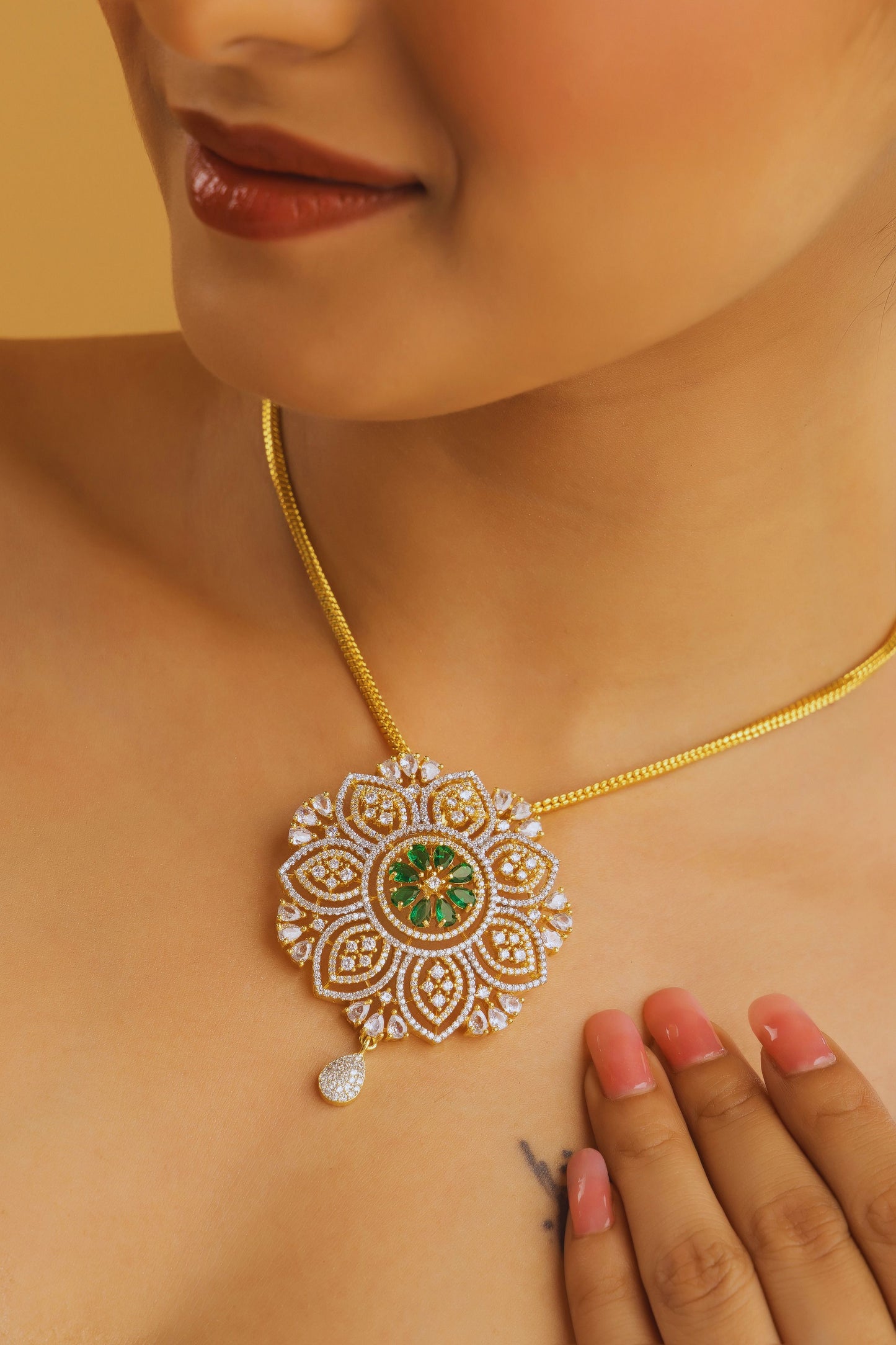 Close-up of a person wearing a gold necklace with a decorative pendant on a beige background