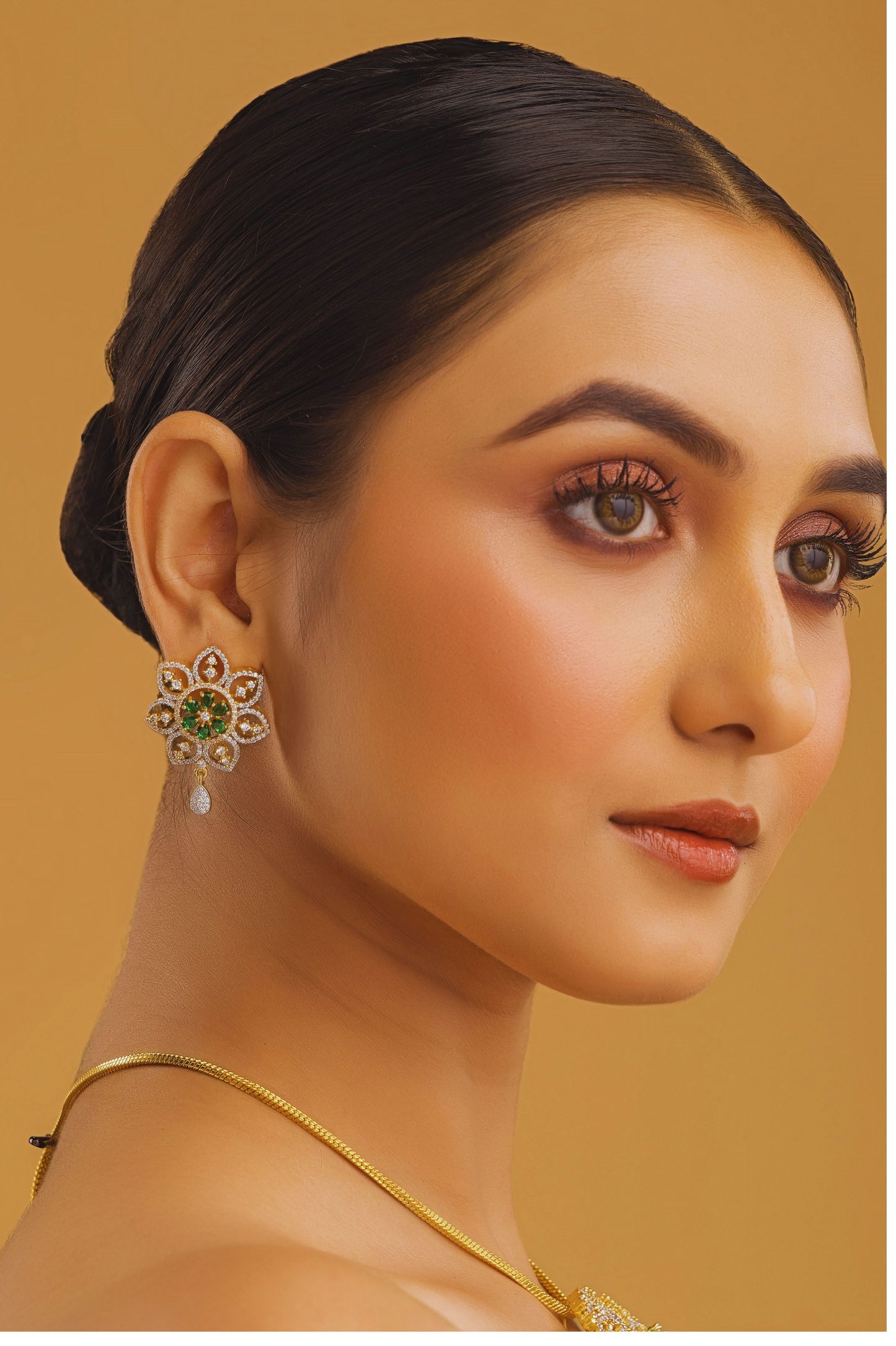 Woman wearing gold earrings with a yellow background