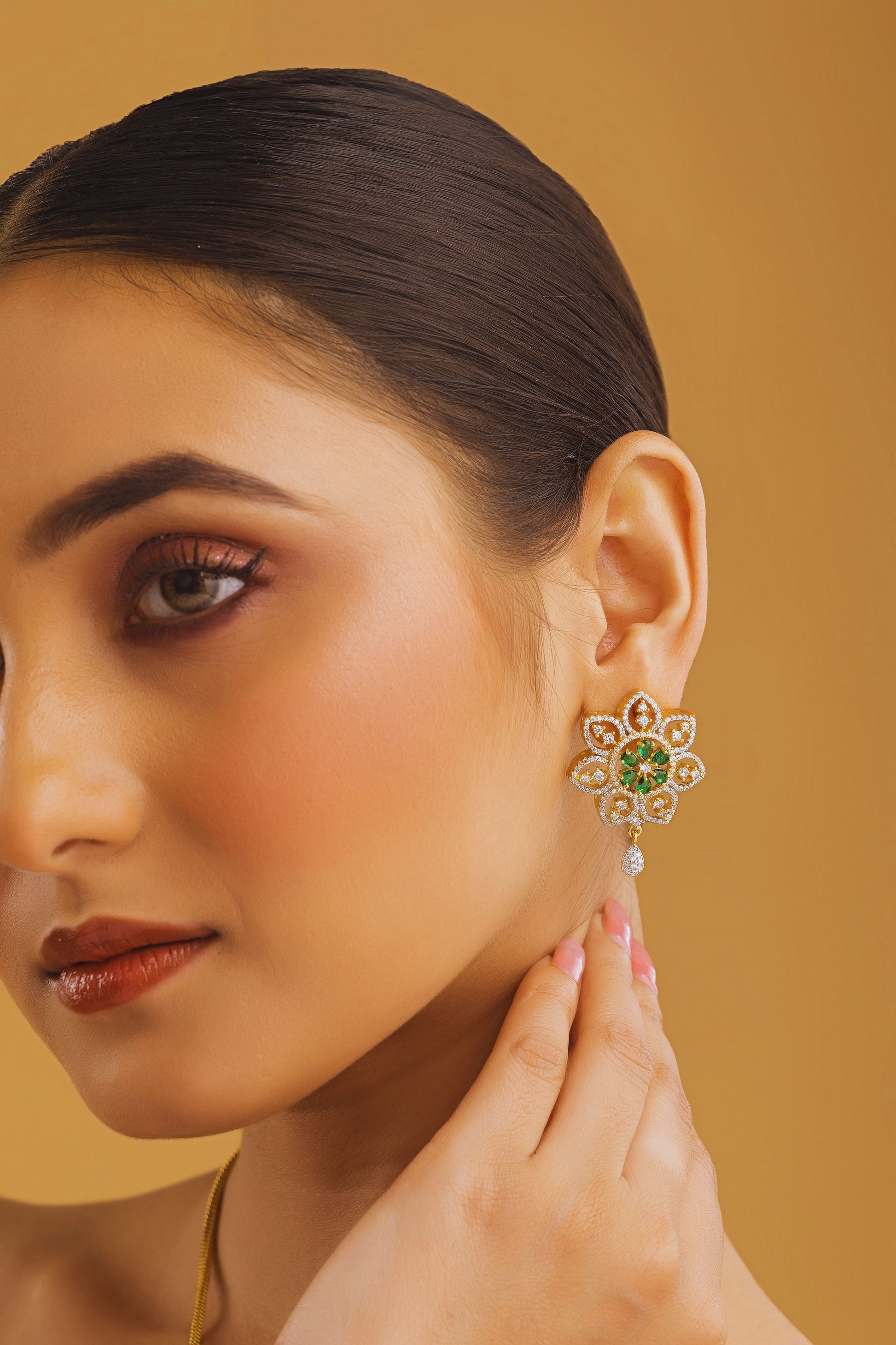 Woman wearing a floral earring with a green gemstone on a beige background
