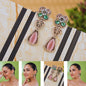 Ornate earrings with pink and green stones on a marble surface, with a model wearing the earrings.