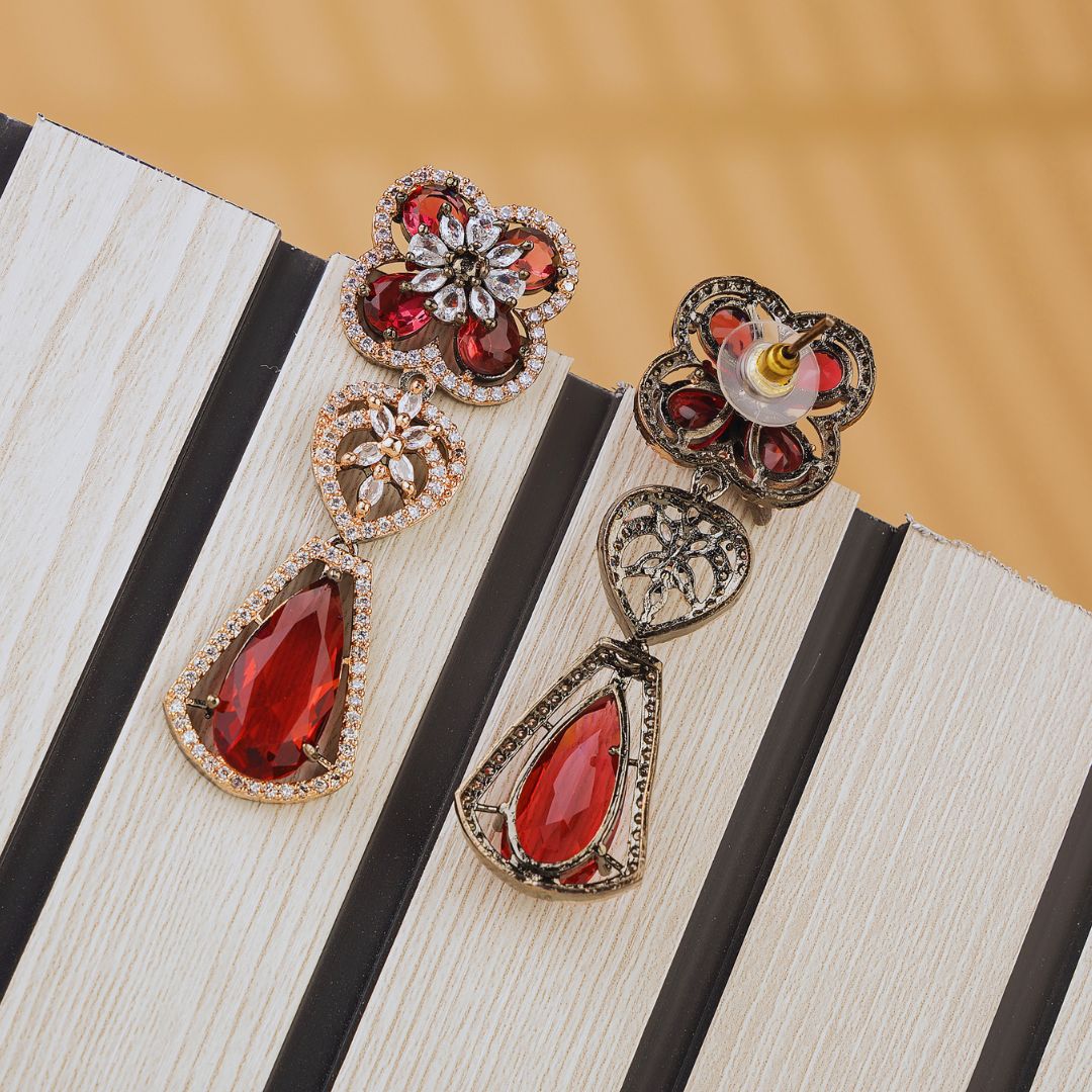 Pair of ornate earrings with red gemstones on a striped surface