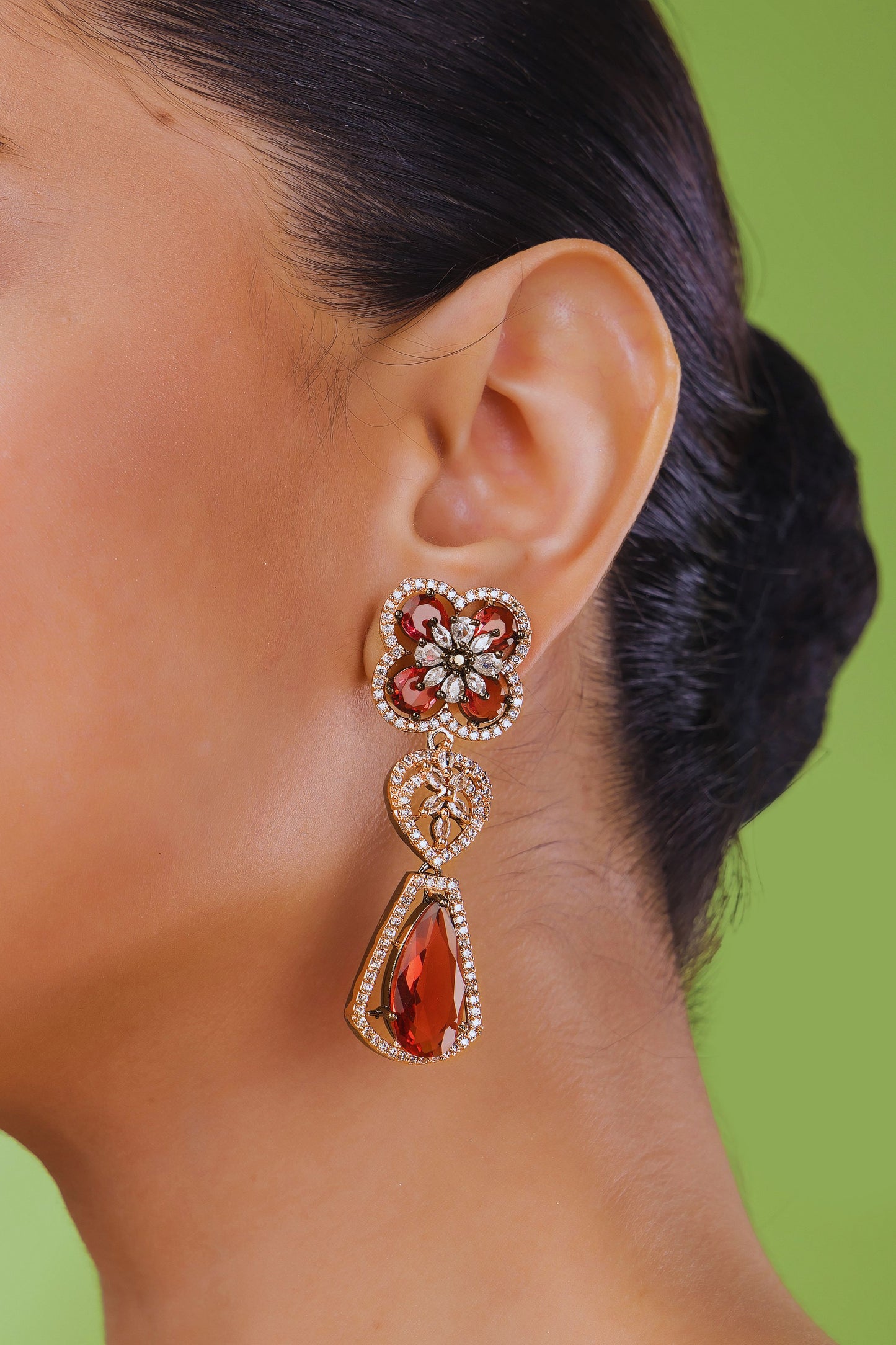 Close-up of a person wearing a pair of ornate earrings with red gemstones on a green background