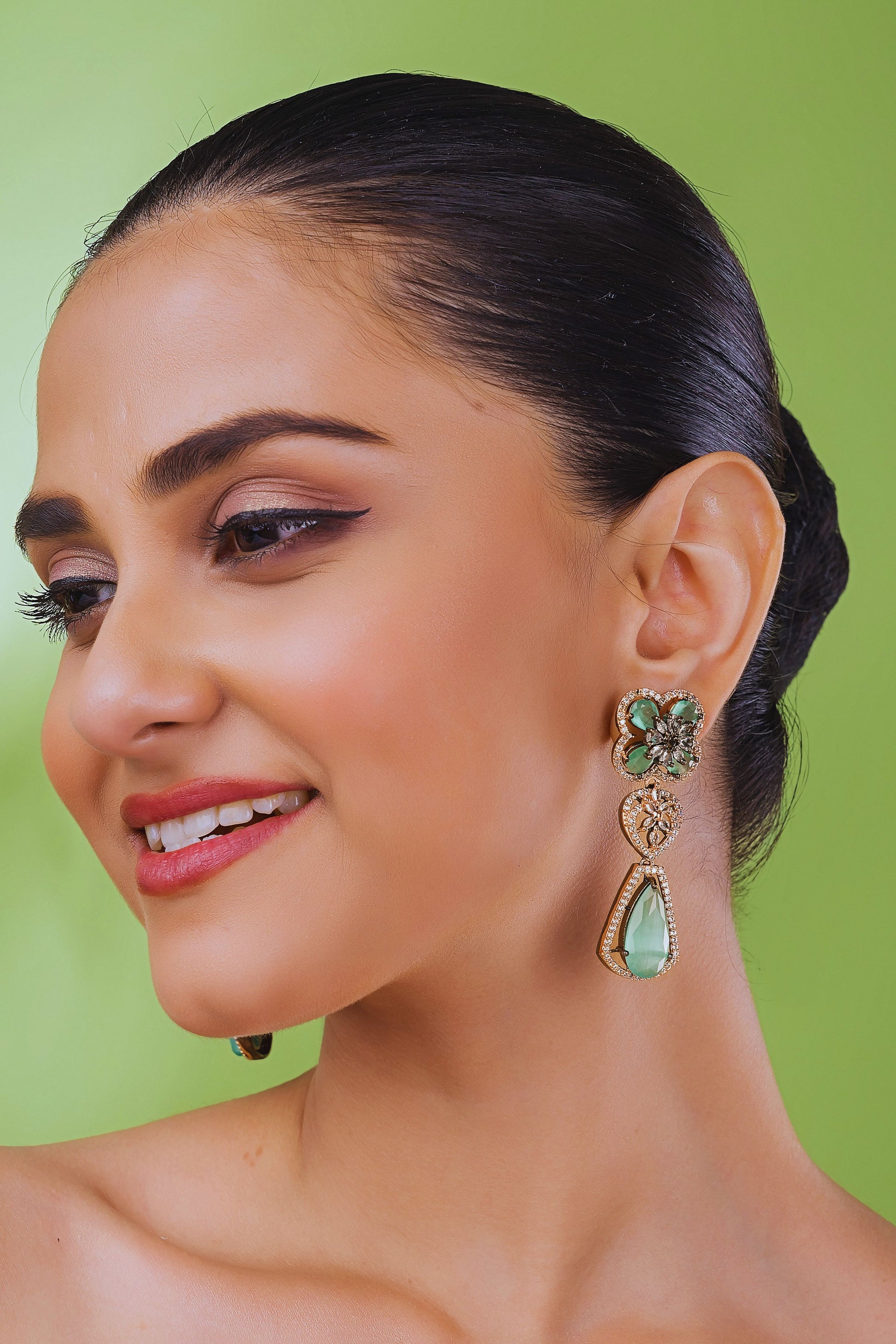 Woman wearing green and gold earrings against a green background