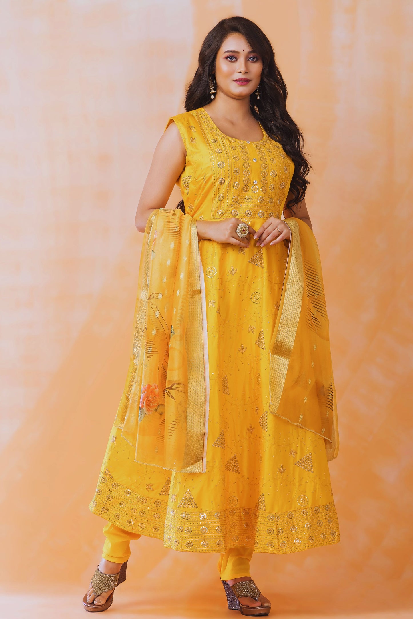 Woman wearing a yellow traditional outfit with a matching dupatta against an orange background