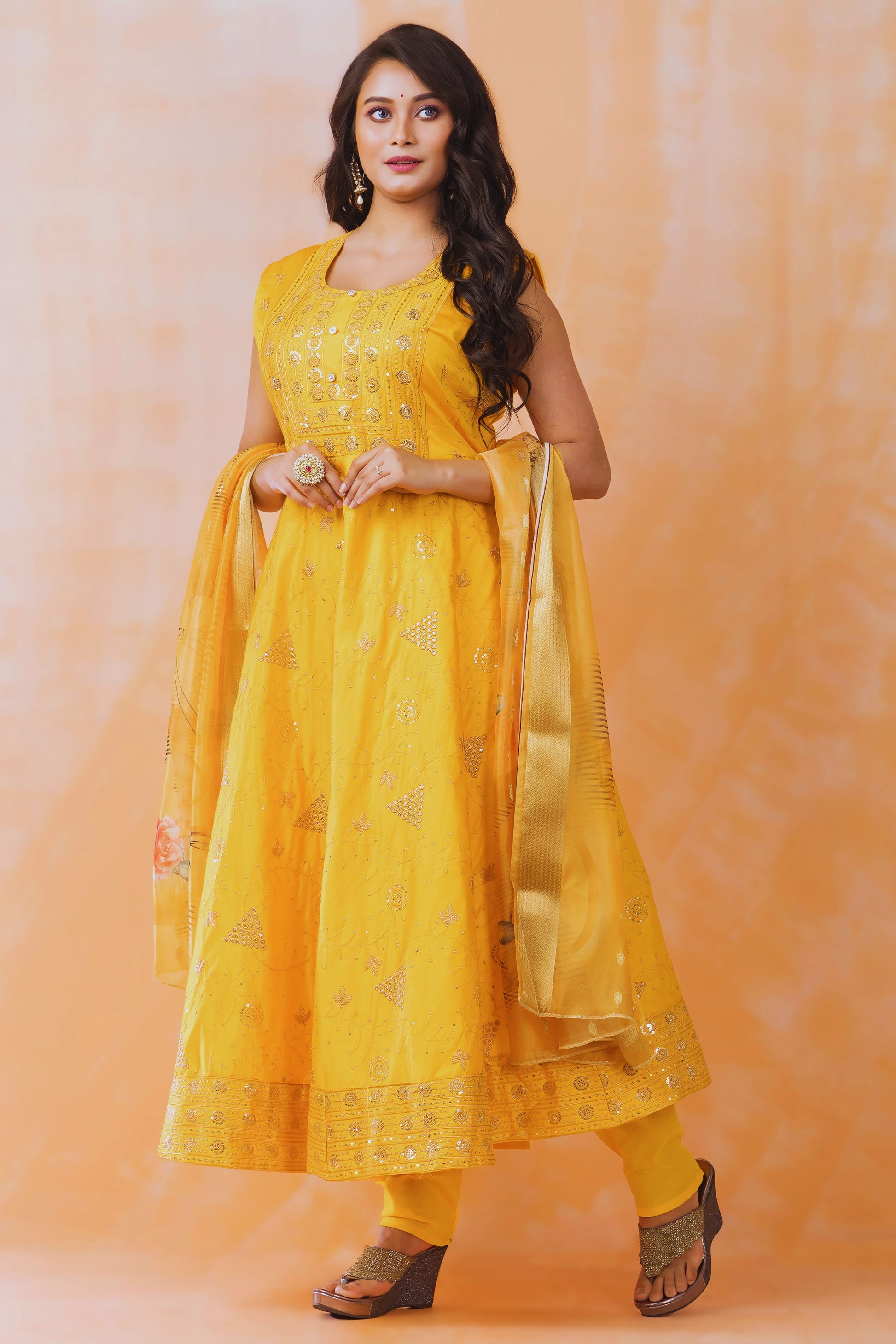 Woman wearing a yellow traditional outfit with a matching dupatta against an orange background
