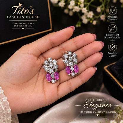 Stud earrings for women featuring pink American diamond floral crystal drop design. A hand holding a pair of silver-toned dangle earrings with clear stones and pink gemstone drops, set against a dark background with a black gift box and decorative text overlays.