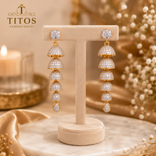 Gold and diamond earrings on a TITOS branded stand with a soft focus background.