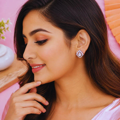 A woman with long dark brown hair is shown in profile wearing a sparkling silver and white floral stud earring against a soft pink background.