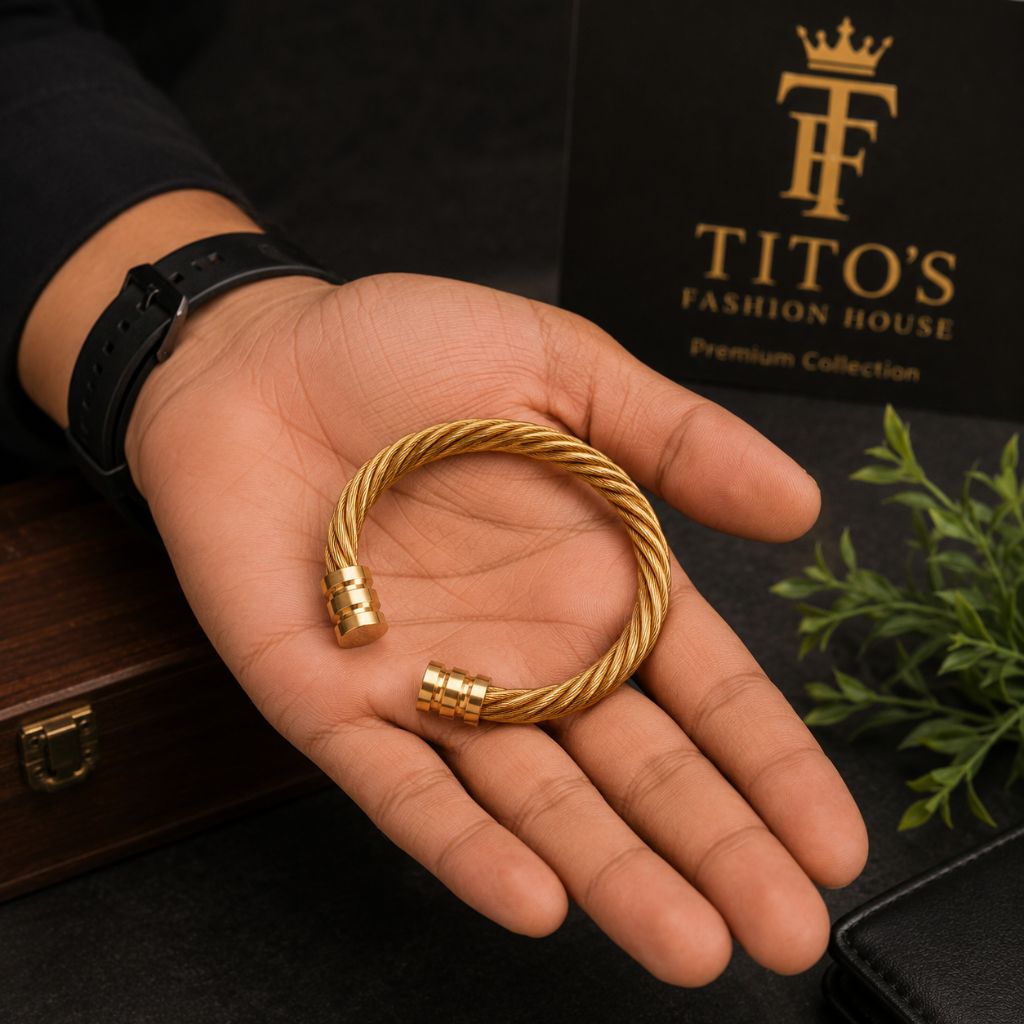 A gold-toned twisted cable bracelet held in a person's hand, with a black TITO'S FASHION HOUSE branded box and dark background visible behind it.