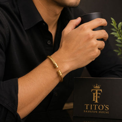 A man wearing a gold twisted rope bracelet with a gold clasp, holding a black mug next to a black gift box branded 'TITO'S FASHION HOUSE'.