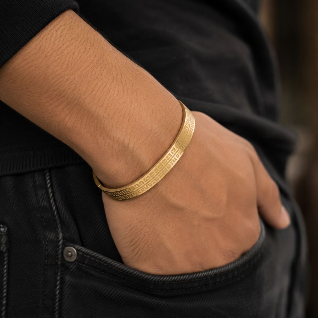 A close-up of a person's hand in a black denim pocket wearing a textured gold bangle bracelet.