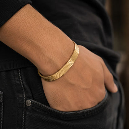 A close-up of a person's hand in a black denim pocket wearing a textured gold bangle bracelet.