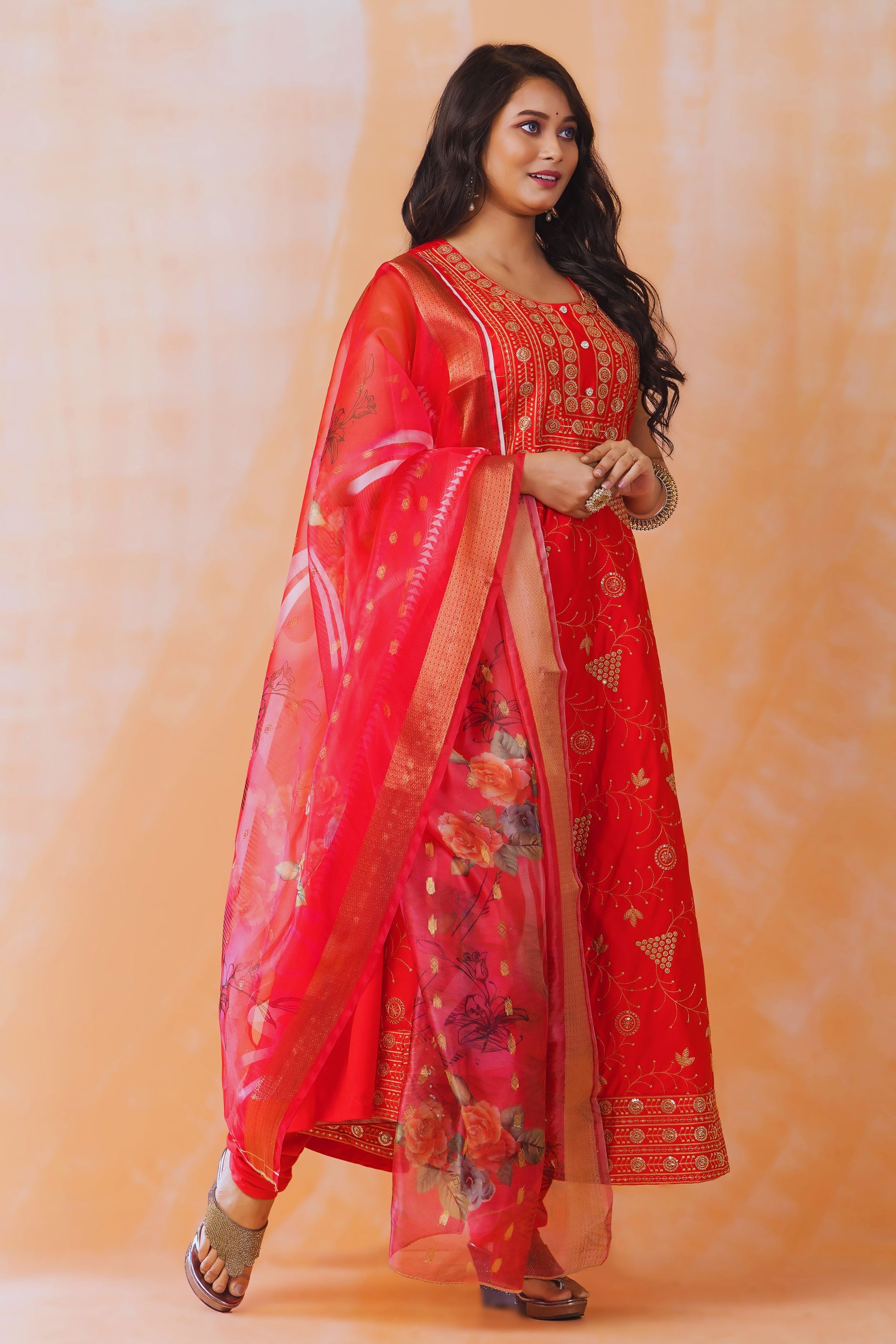 Woman wearing a red traditional outfit with a matching dupatta against an orange background