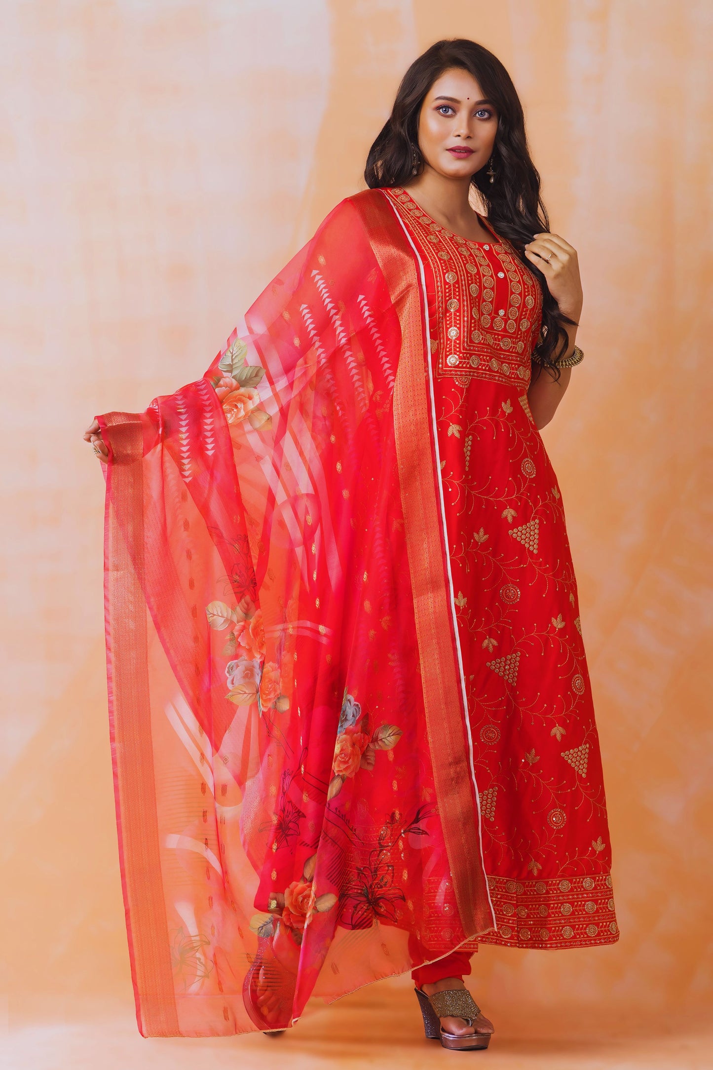 Woman wearing a red traditional outfit with a matching dupatta against an orange background