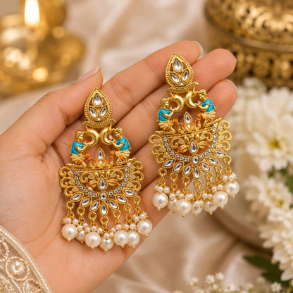 Gold earrings with pearls held in a hand against a blurred decorative background