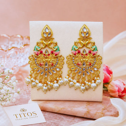 Ornate gold earrings with pearls on a beige card, with 'TITOS' branding visible.