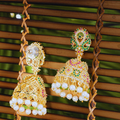 Gold earrings with pearls and gemstones on a woven background