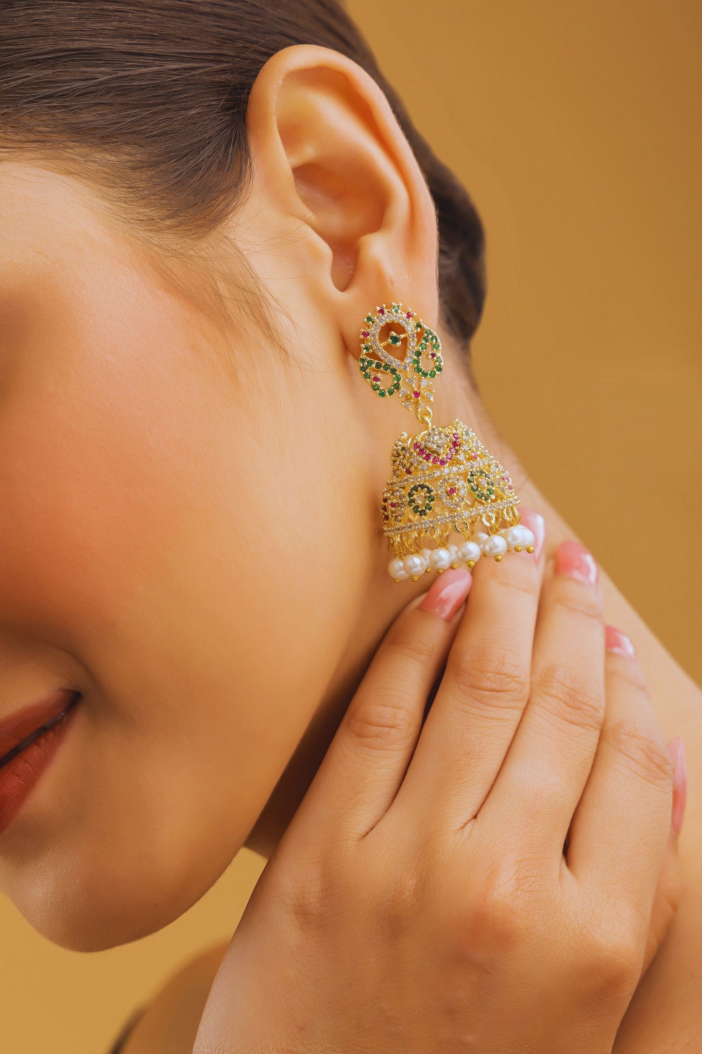 Close-up of a woman wearing a gold and gemstone earring against a warm background
