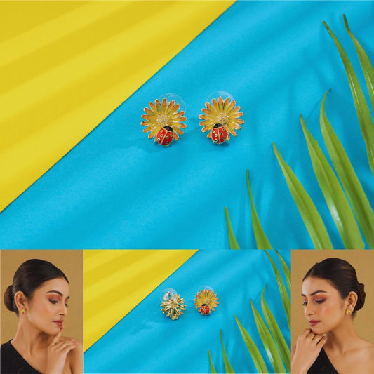 Gold earrings with red berries and green leaves on a blue and yellow background with grass.