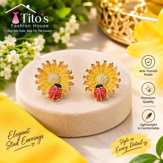 A pair of ladybug stud earrings displayed on a round beige pedestal. The earrings feature a gold-tone metal base with a yellow sunflower petal design and a red ladybug with black spots and small clear rhinestones.