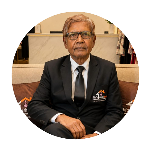 A circular portrait of an older man wearing glasses, a black suit, white shirt, and black tie, seated indoors. A small logo patch is visible on the left chest of the suit.