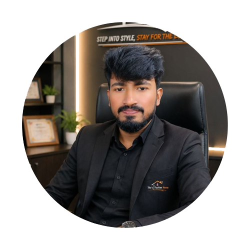 A man with a beard and black hair wearing a black blazer over a black button-down shirt, sitting in a black office chair. The photo is framed in a circular border on a white background, with a dark office interior visible behind him.