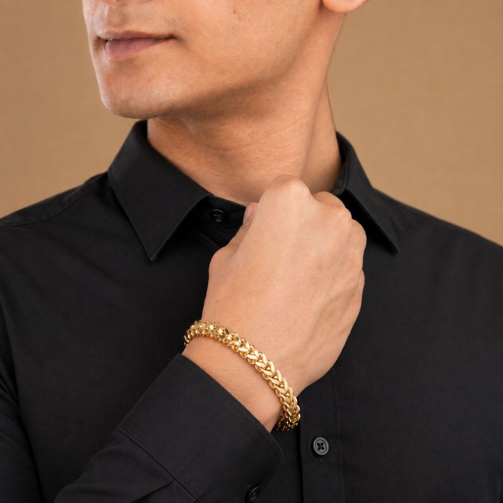 A close-up of a man wearing a thick gold chain bracelet on his wrist, dressed in a black collared shirt against a warm beige background.
