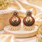 Ornate earrings with green and red design on a beige surface with flowers.