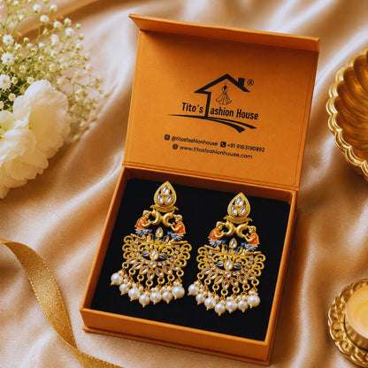 Gold and pearl earrings in a Tito's Fashion House box on a beige fabric background with flowers.