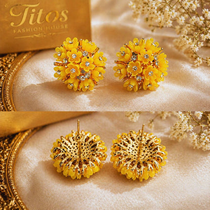 Yellow floral earrings with gold accents on a beige fabric background, branded 'Titos Fashion House'.