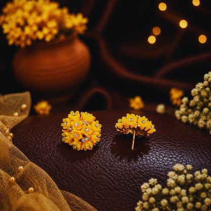 Yellow floral earrings on a dark surface with blurred lights and flowers in the background