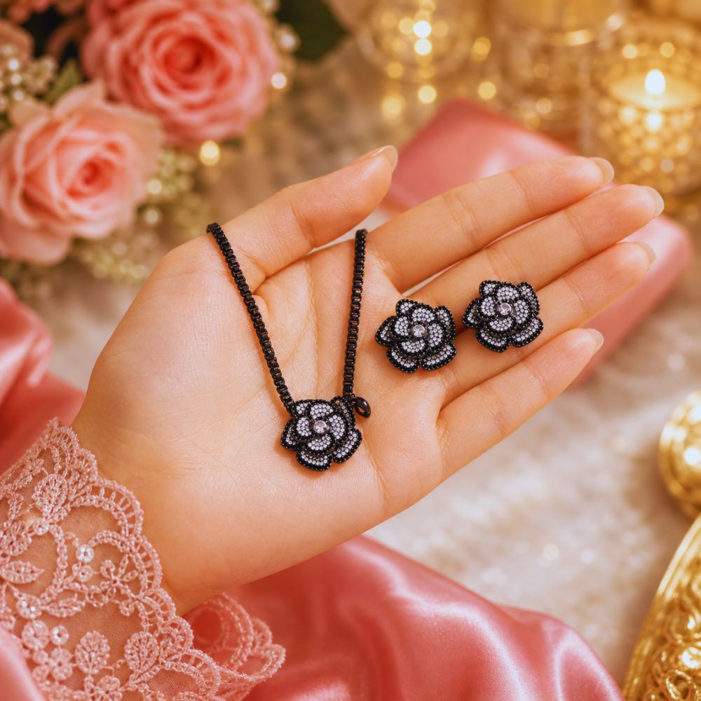 Hand holding black rose-shaped jewelry with pink roses and gold decorations in the background