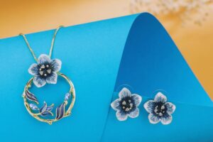 Elegant anti-tarnish floral jewelry set with gold-plated necklace and matching flower stud earrings, featuring enamel detailing and crystal embellishments – displayed on a white background.